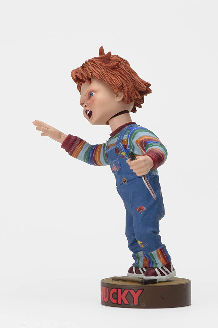 side of Head knocker bobble head of Chucky from Child's Play 2. Chucky has his right hand up, mouth open as if he is yelling, and in his left hand is clutching a knife. Chucky stands on a small round platform that reads "CHUCKY" in red letters on the front.